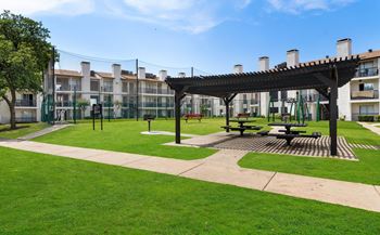a park area with picnic tables and awning in front of an apartment building
